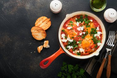 Shakshuka. Ev yapımı sahanda yumurta ve demir tavada sebzeler. Eski koyu levha, taş ya da beton arka plan. Geleneksel İsrail mutfağı. Geç kahvaltı konsepti. Arap mutfağı. Üst görünüm.