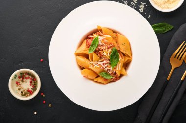 Bolonez Penne Pastası. Siyah arka planda beyaz tabakta parmesan, fesleğen ve bolonez soslu lezzetli İtalyan makarna. Geleneksel İtalyan mutfağı. Üst görünüm.