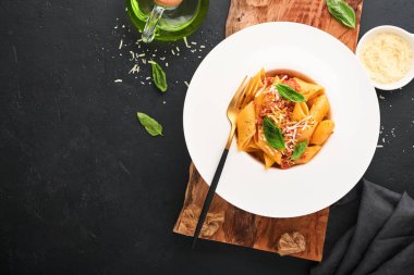 Bolonez Penne Pastası. Siyah arka planda beyaz tabakta parmesan, fesleğen ve bolonez soslu lezzetli İtalyan makarna. Geleneksel İtalyan mutfağı. Üst görünüm.