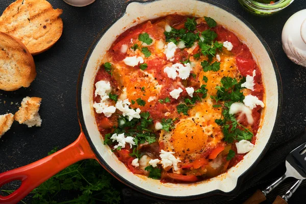 Shakshuka 用铁锅在旧的深色石板 石板或混凝土背景上自制的煎蛋和蔬菜 以色列的传统美食 深夜早餐的概念 阿拉伯菜 顶部视图 图库照片