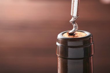 Tirbuşonlu bir şişe şarap. Restoranda tirbuşonla şarap şişesi açmak. Fotokopi uzayı olan koyu kırsal arkaplanda şarap kompozisyonu. Model.