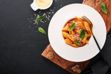 Bolonez Penne Pastası. Siyah arka planda beyaz tabakta parmesan, fesleğen ve bolonez soslu lezzetli İtalyan makarna. Geleneksel İtalyan mutfağı. Üst görünüm.