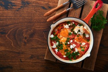 Shakshuka. Domates, zeytinyağı, biber, soğan ve sarımsak soslu ev yapımı sahanda yumurta eski ahşap arka planda demir kızartma tavasında. Geleneksel İsrail mutfağı. Geç kahvaltı konsepti.