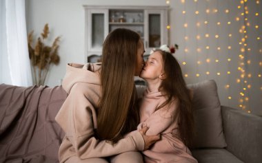 Anne ve kızı kanepede oturup öpüşüyorlar.