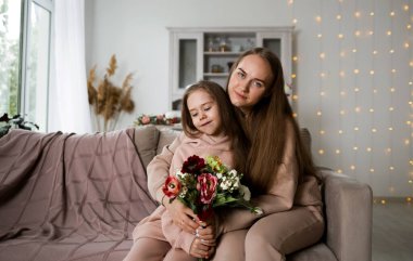 Sweatshirt giymiş güzel bir anne ve kız kanepede çiçeklerle oturuyor.