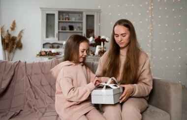 Güzel anne ve kızı kanepeye oturmuş hediye kutusuyla onu açıyorlar.