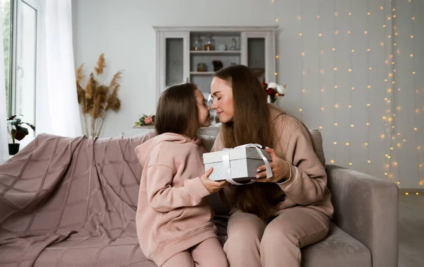 Anne ve kızı kanepeye oturmuş, hediye kutusuyla öpüşüyorlar.