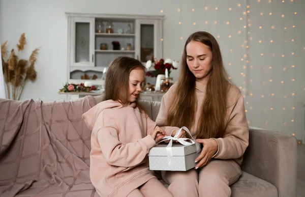 Güzel anne ve kızı kanepeye oturmuş hediye kutusuyla onu açıyorlar.