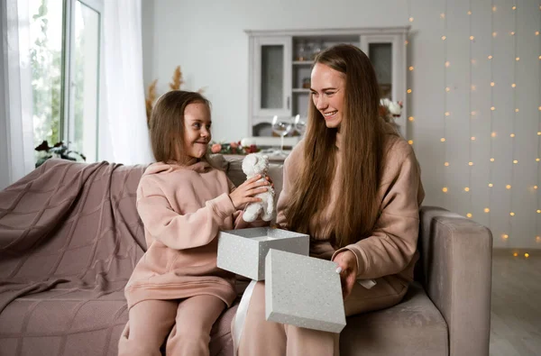 Mutlu bir anne ve kız kanepeye oturmuş hediye kutusuyla onu açıyorlar.