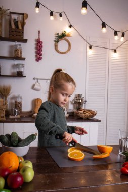 Yeşil kazaklı sarışın bir asistan masada oturuyor ve bir portakal kesiyor.