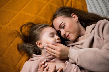 Anne yatakta uzanıyor ve kızının yanağını okşuyor.