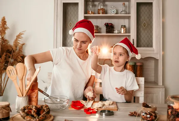 クリスマスの帽子の美しい母親と娘がキッチンのテーブルに座り — ストック写真