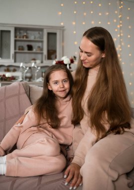 Aynı takımları giyen güzel bir anne ve kız odadaki kanepede oturuyorlar.