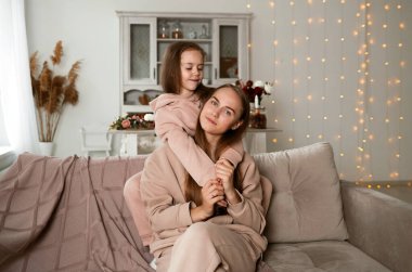 Kızı kanepede oturuyor ve annesine sarılıyor.