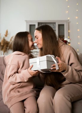Küçük bir kız ve anne kanepede oturuyor ve bir hediye veriyorlar.