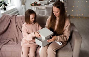 Güzel anne ve kızı kanepede oturuyor ve bir hediye açıyor.