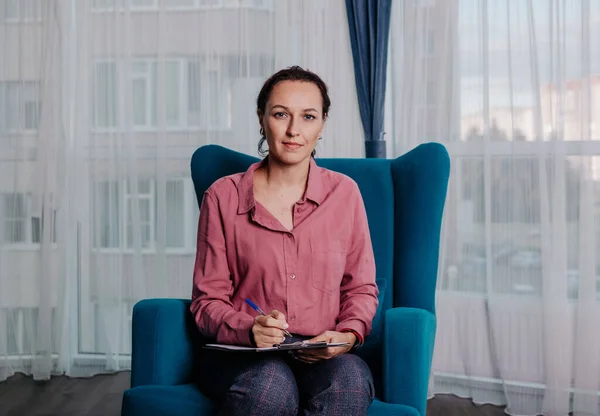 Bir kadın psikolog odada bir sandalyede oturuyor.