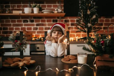 Yeni yıl şapkalı küçük bir çocuk masada oturuyor ve elinde renkli lolipoplar tutuyor.