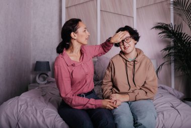 İletişim kuran esmer bir anne ve genç bir kız odada yatakta oturuyor.