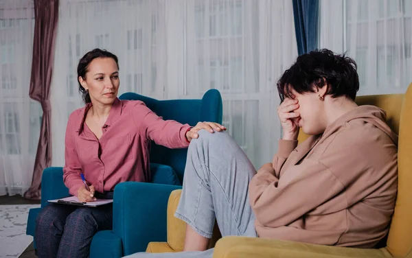 a female psychologist sits in a chair and consults a teenage girl in a room