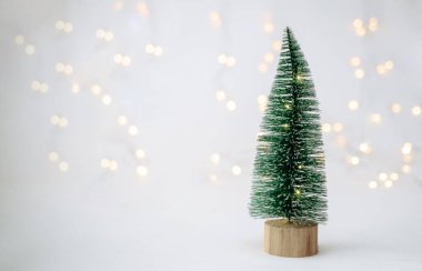 Beyaz arka planda küçük yapay bir Noel ağacı. Üzerinde yazacak yeri olan bir çelenk var.