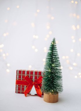 Beyaz arka planda yeni yıl hediyesi olan küçük yapay bir Noel ağacı ve mesaj için yeri olan bir bokeh.