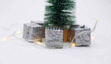 Beyaz bir arka planda, bir Noel ağacının altında küçük gümüş folyo hediyelerin yakın plan çekimleri ve metin için bir yer