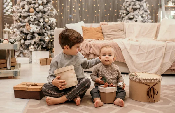 小さな男の子たちがクリスマスツリーを背景に贈り物を持って部屋のカーペットの上に座っています — ストック写真