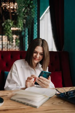 Mutlu bir iş kadını bir kafedeki masada telefonla iletişim kurar.