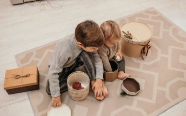 Küçük çocuklar, Noel ağacının arka planında hediyelerle bir odada halının üzerinde oturuyorlar.