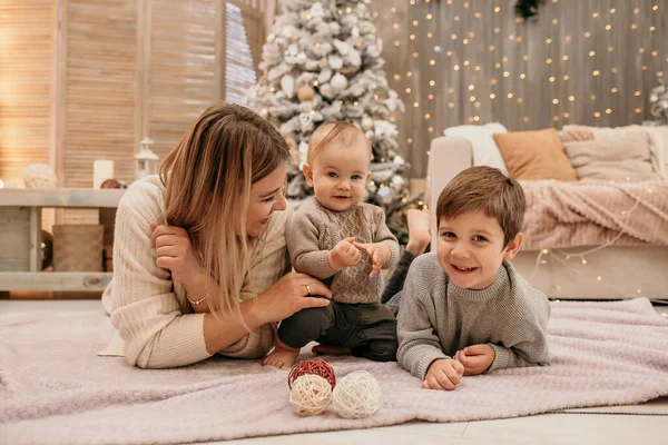 若い息子とブロンドのお母さんは部屋のクリスマスツリーの近くの毛布の上に座っている — ストック写真