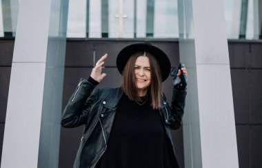 Siyah elbiseli ve deri ceketli agresif genç bir kadın sokakta dikiliyor.
