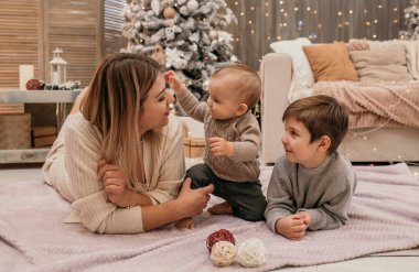 Anne ve oğulları Noel ağacının yakınındaki bir odada battaniyenin üzerinde uzanıyorlar ve iletişim kuruyorlar.