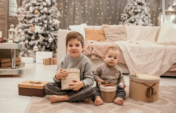 幸せな2人の兄弟はソファの近くに座ってクリスマスツリーの周りにギフトで抱き合っています — ストック写真