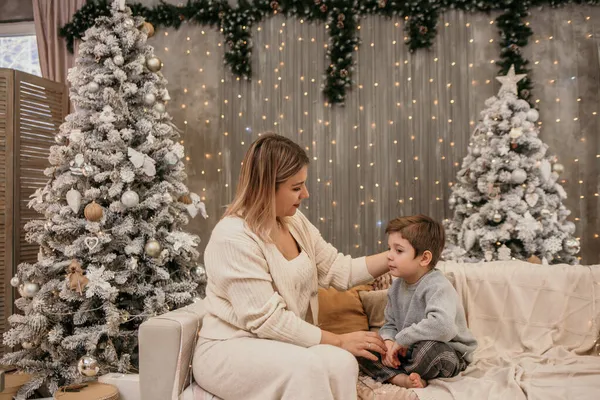 若い母親がソファに座って息子のトッドとクリスマスツリーの近くの部屋で話してる — ストック写真