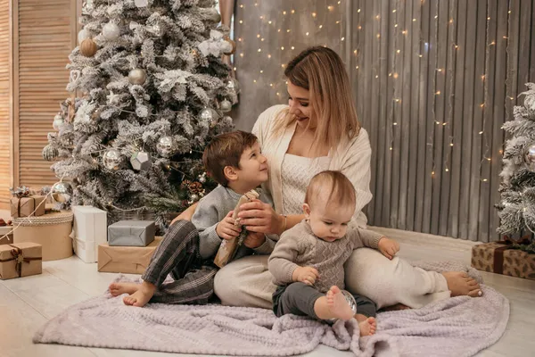 幸せなお母さんと息子は床に座ってクリスマスツリーの近くの部屋でおしゃべりしています — ストック写真