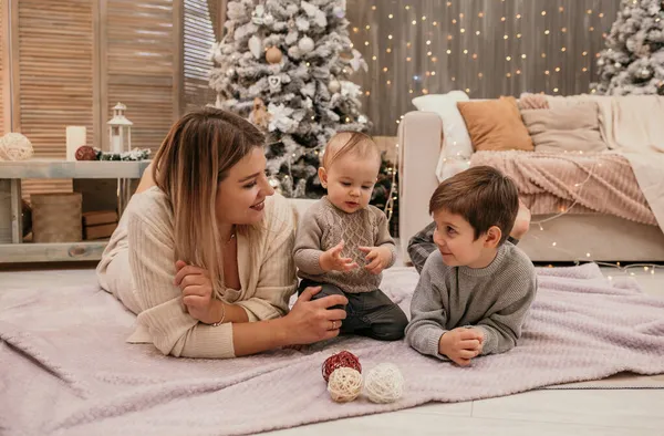 お母さんと息子は部屋の毛布の上に横になってクリスマスツリーの周りで話しています — ストック写真