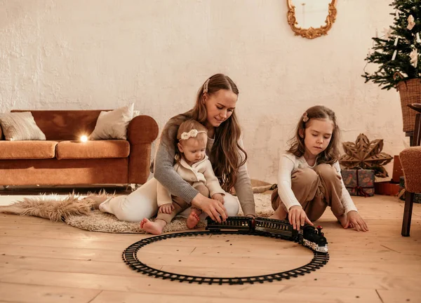 部屋のカーペットに座って電車で鉄道と遊んでいる美しいお母さんと娘たち — ストック写真