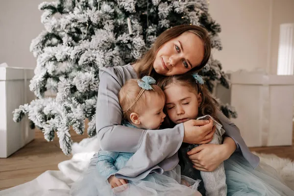 クリスマスツリーの近くに座って抱きかかえている娘を持つ母親の肖像画 — ストック写真