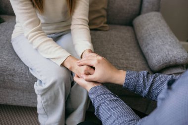 Hastanın ellerine sarılan bir kadın doktorun yakın çekimi. Bir destek jesti. Bir kadına psikolojik yardım