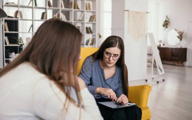 Özenli bir psikolog odada bir resepsiyon düzenler ve bir kadın hastayı dinler. Profesyonel psikolojik yardım