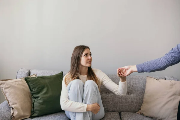 Üzgün bir kadın kanepede oturuyor ve yardım elini uzatmayı kabul ediyor. Aile içi şiddetle mücadele