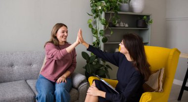 Mutlu bir kadın psikolog bir sandalyede oturmuş bir hastayla çözülmüş bir problemi kutluyor. Başarılı psikoterapi