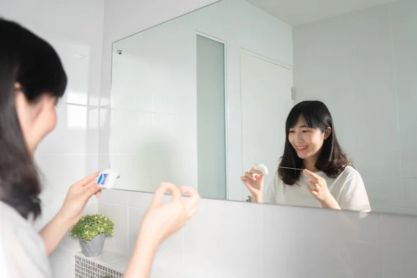 Young asian woman cleaning teeth with dental floss after brushing her teeth in bathroom. Oral hygiene routine for freshness breath, prevent plaque and gum disease. Dental health care concept.
