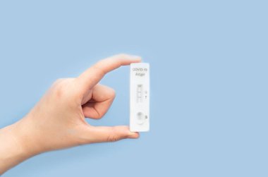 SARS CoV-2 Rapid Antijen Test kiti (ATK) taşıyan kadın elleri mavi arka planda COVID-19 testi sırasında pozitif sonuç verdi.