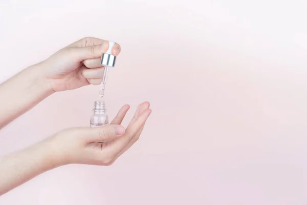 Skin care routine. Woman hands holding cosmetic glass bottle with dropper on pink background. Products of serum or essential oil. Aromatherapy, spa and beauty concept.
