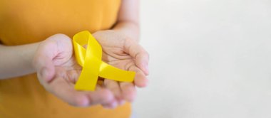 Endometriyozis, intihar önleme, sarkoma kemiği kanseri, mesane kanseri, karaciğer kanseri ve çocukluk kanseri konsepti için sarı altın kurdele farkındalığı sembolü taşıyan genç bir kadın. Sağlık hizmetleri. Boşluğu kopyala.