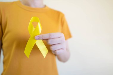 Endometriyozis, intihar önleme, sarkoma kemiği kanseri, mesane kanseri, karaciğer kanseri ve çocukluk kanseri konsepti için sarı altın kurdele farkındalığı sembolü taşıyan genç bir kadın. Sağlık hizmetleri. Boşluğu kopyala.