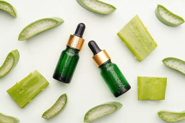 Natural moisturizer skincare product with fresh aloe vera on green background. Serum or essential oils with organic herbal extract in glass bottle for healthy skin. Dermatology and medicine concept.