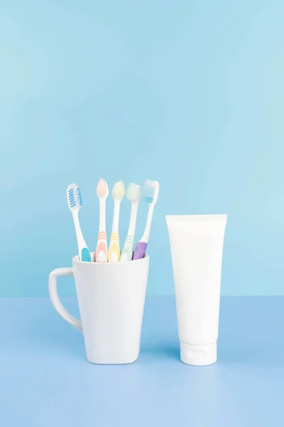 Toothbrushes in a glass and toothpaste tube with empty label on light blue background. Dental health care and oral hygiene concept. Mock up.